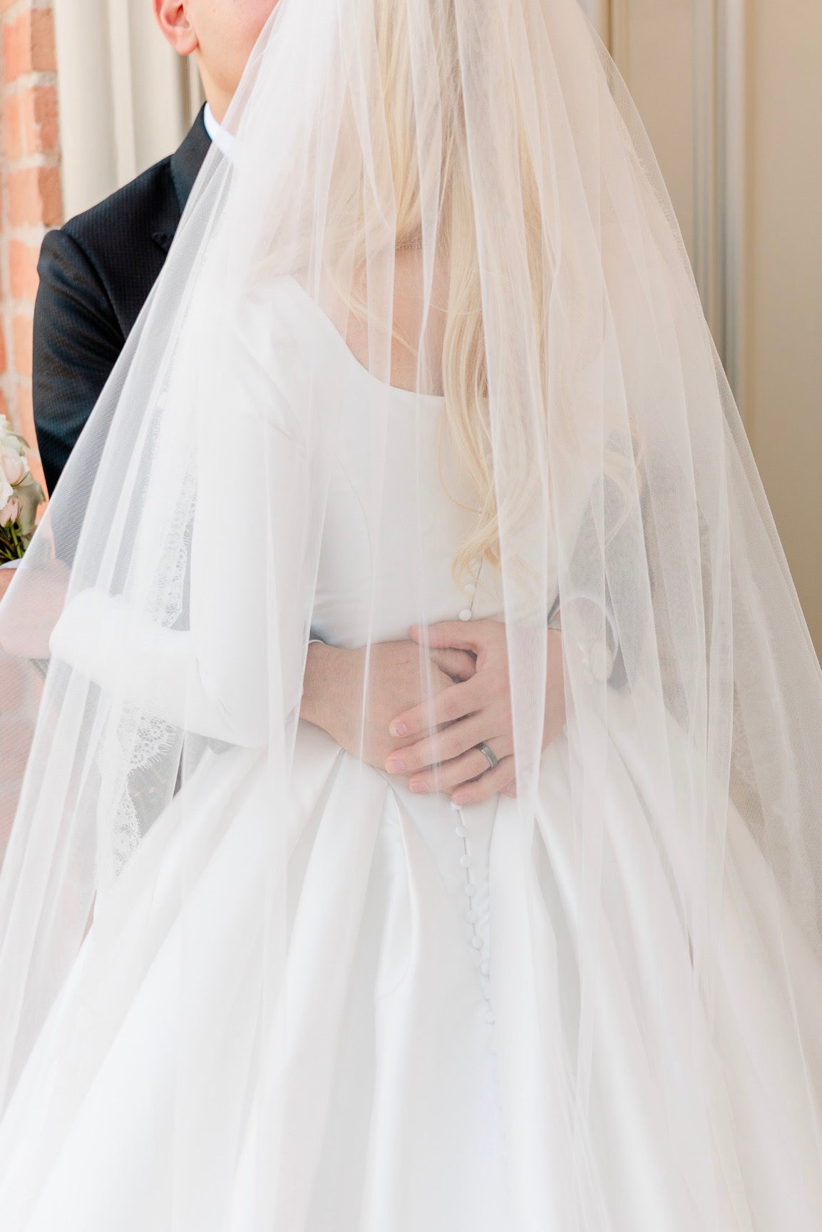 Person in a wedding dress with a veil, standing next to a person in a suit.